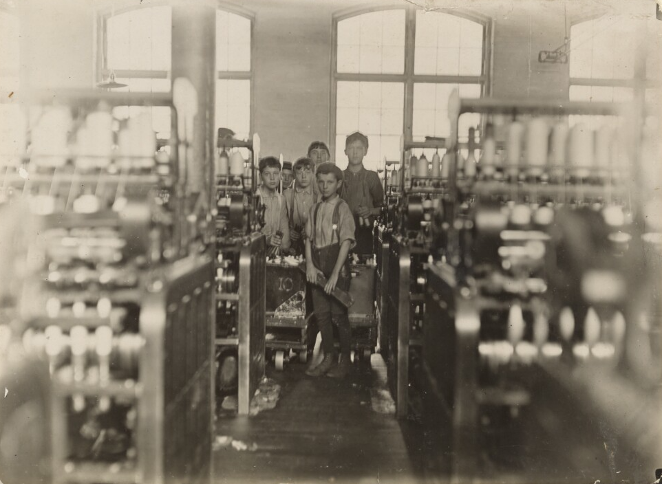 Black and white photo of a group of boys in a mill surrounded by large machines