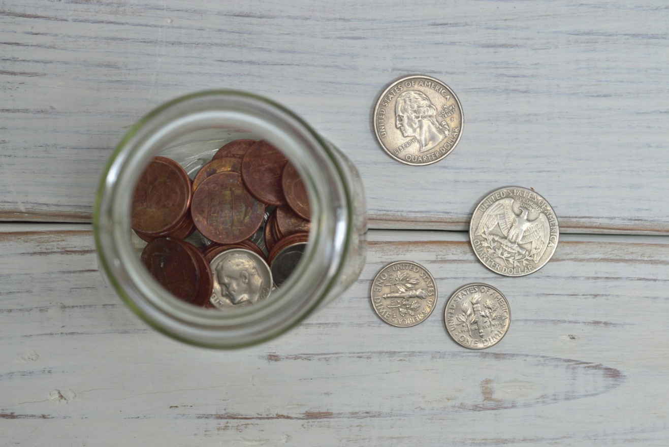 A tip jar filled with coins and a couple of them spread outside.