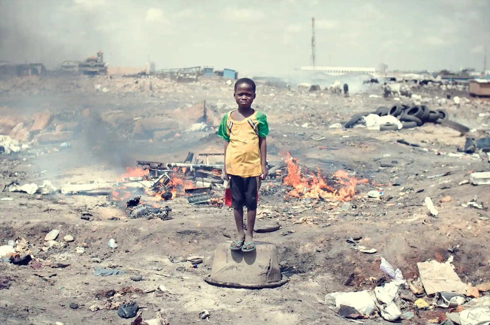 A Ghanaian child, Kwabena, standing in the middle of piles of e-waste in Agbogbloshie, Ghana.