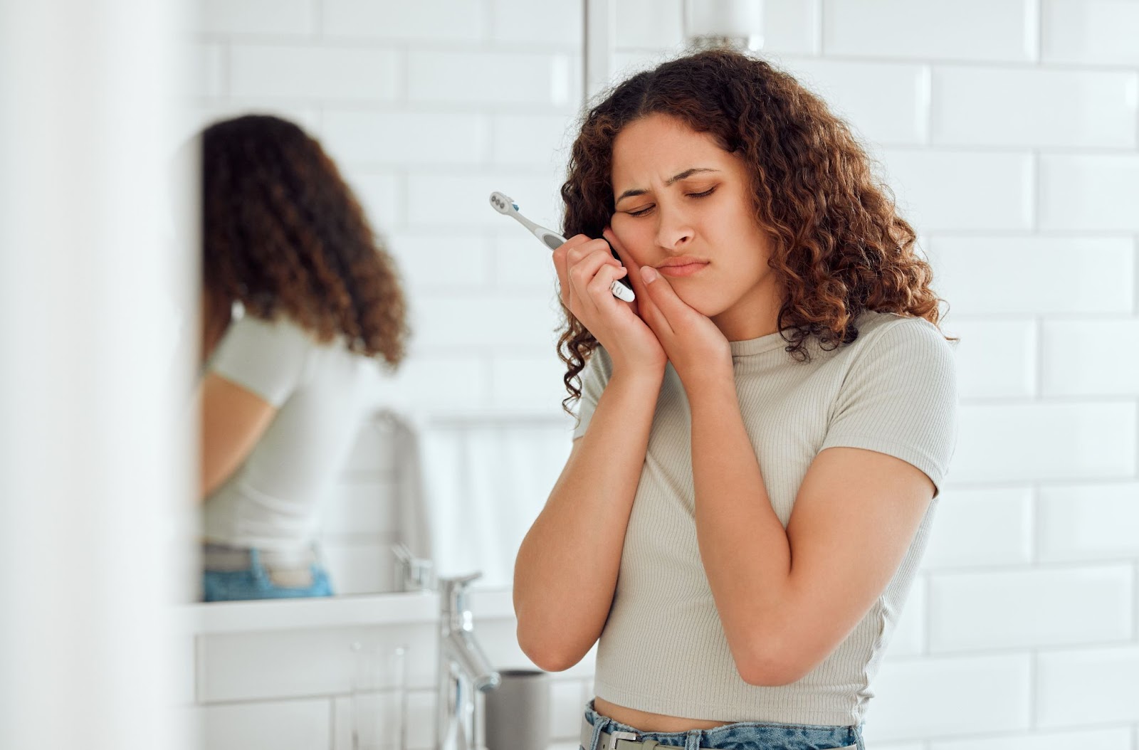 Woman holding the side of her jaw in pain while brushing her teeth from a cavity that's been left untreated.
