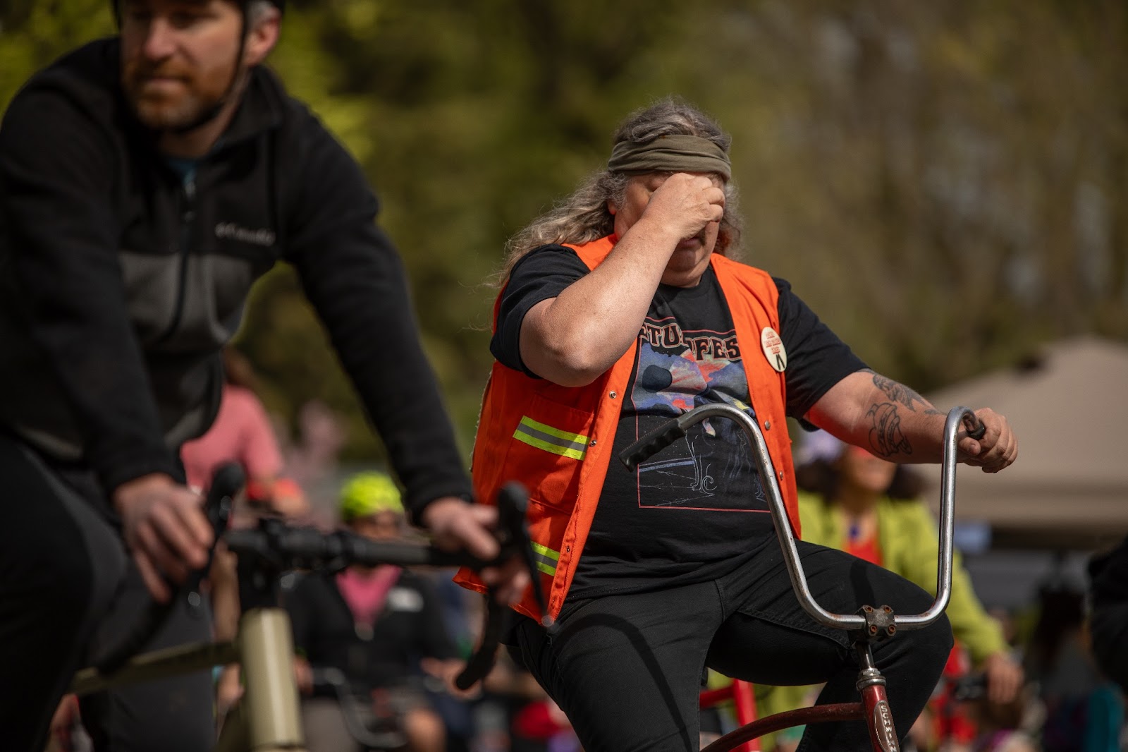 A tattooed man in black jeans and an orange safety vest riding a bike with the old-timey cruiser handlebars in the Ladd's 500 relay in Portland.