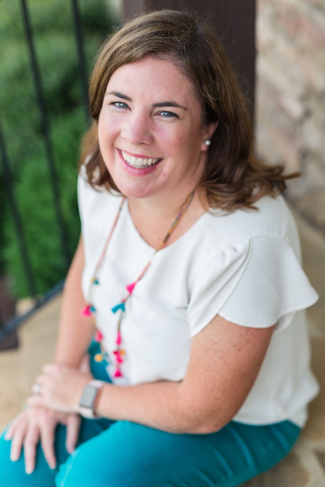 Cameron smiles for the camera in a white blouse and turquoise pants as she sits upon the front stoop of her home.