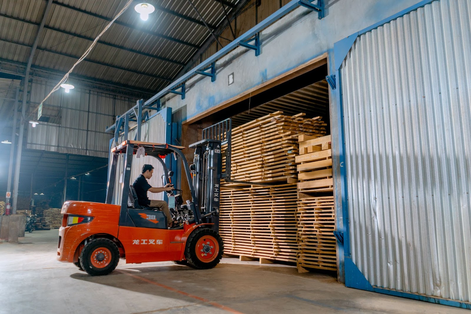 A person wheeling a forklift through a warehouse and picking up wood pallets